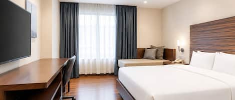 Hotelkamer met een bed, een bureau met stoel, een televisie en een raam met gordijnen.
