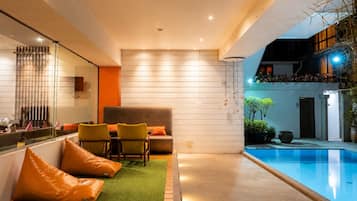 Zona interior de piscina moderna con área de descanso, una partición de cristal y piscina con borde azul transparente.