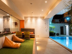 Zona interior de piscina moderna con área de descanso, una partición de cristal y piscina con borde azul transparente.
