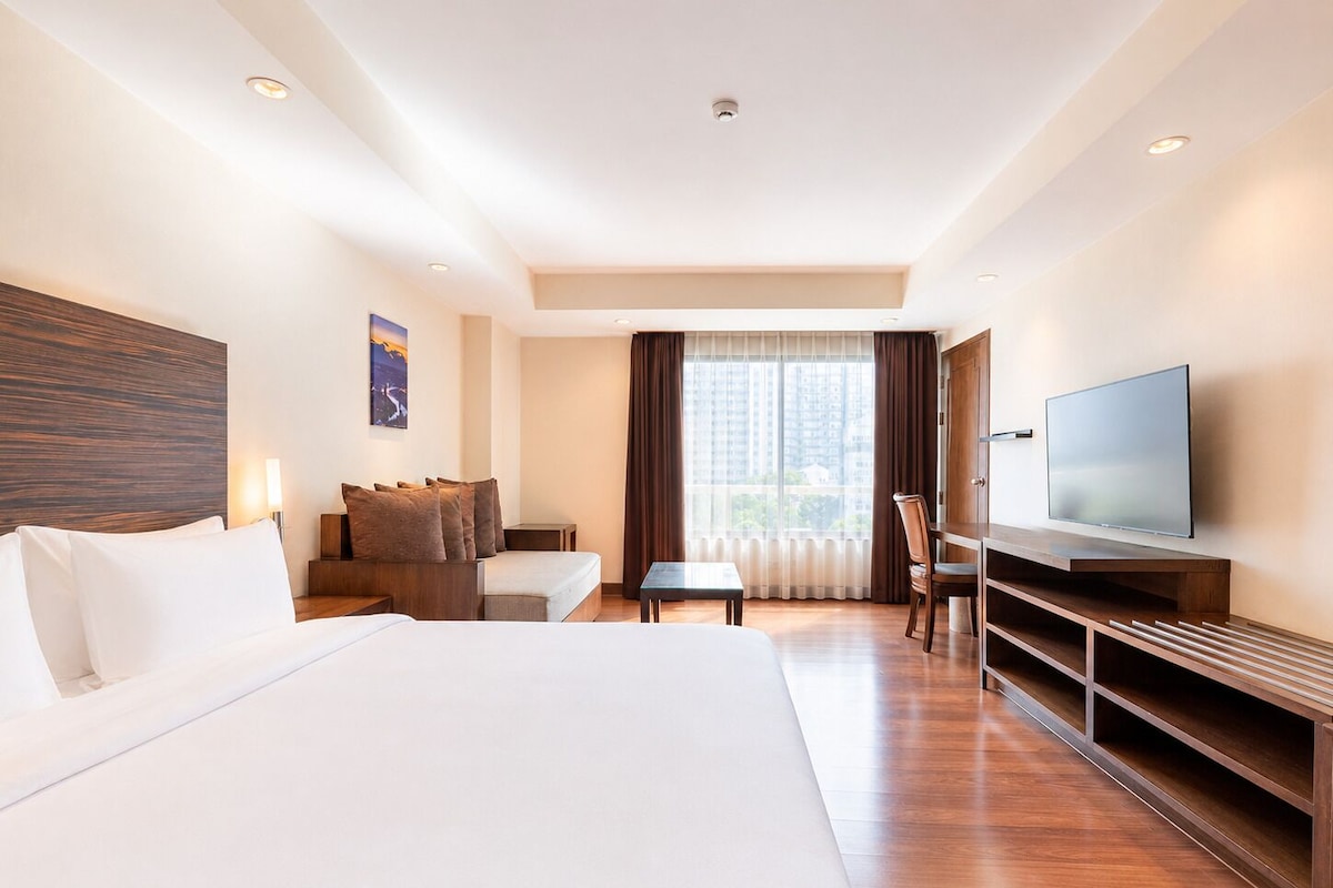 Habitación de hotel con una cama grande, un escritorio, una silla, un televisor y una ventana con cortinas.