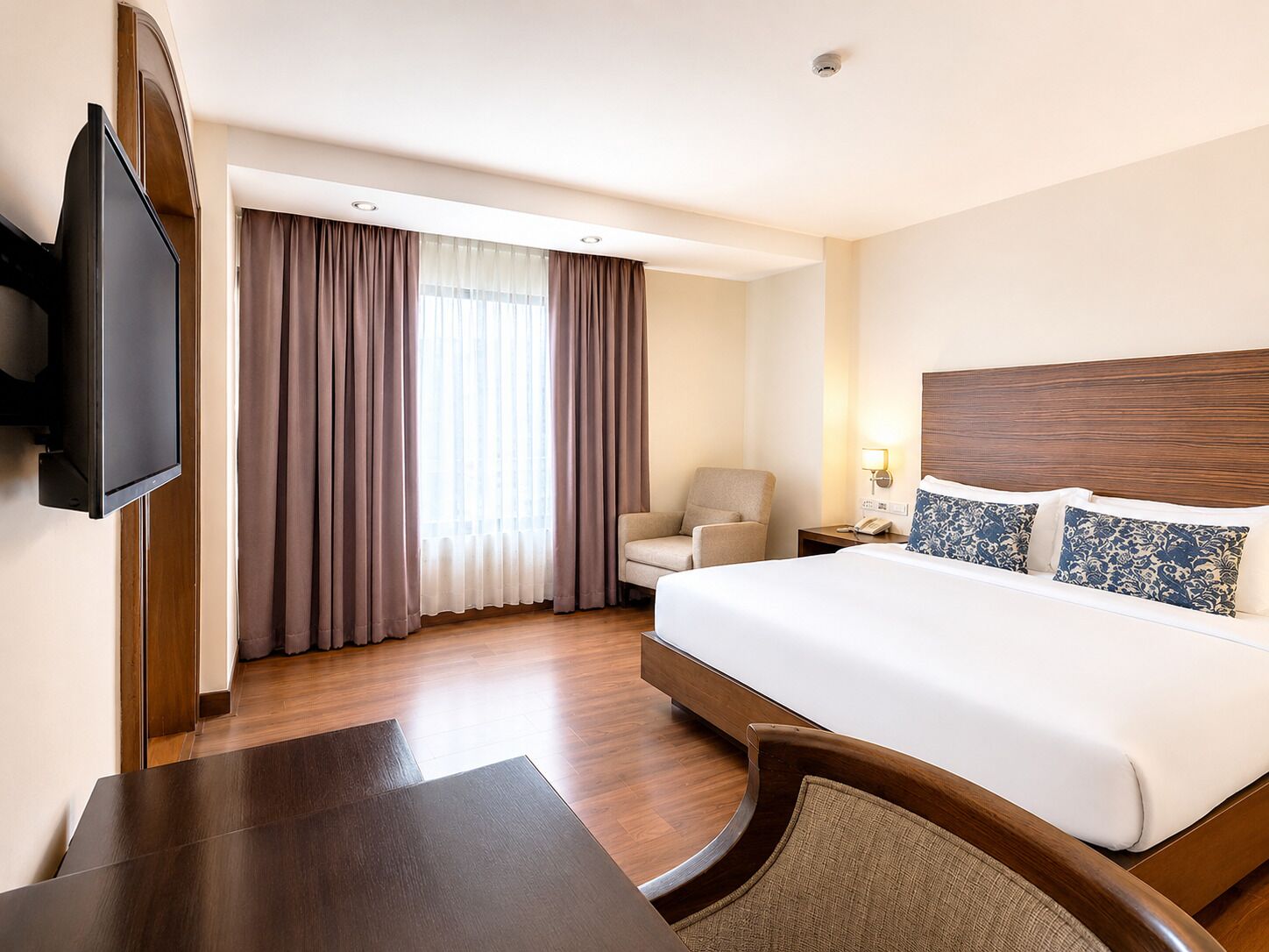 A hotel room with a bed, a desk, a chair, a TV, and a window with curtains.