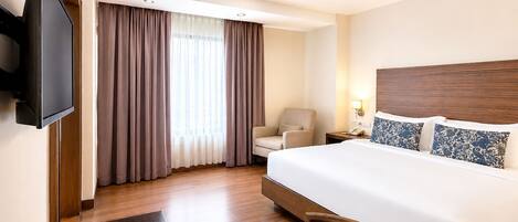A hotel room with a bed, a desk, a chair, a TV, and a window with curtains.