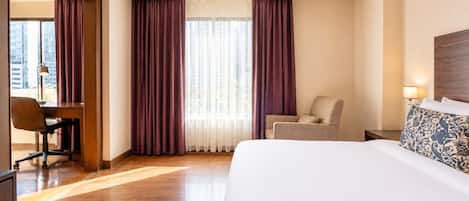 Una habitación de hotel con una cama grande, un escritorio con una silla y vistas a la ciudad desde la ventana.