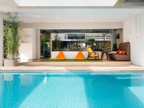 Un área de piscina interior moderna con vista despejada, una zona de estar con cojines y una planta en maceta.