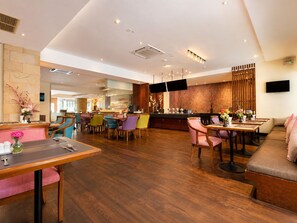 Un hall de hotel con bar, zonas de estar y una televisión.