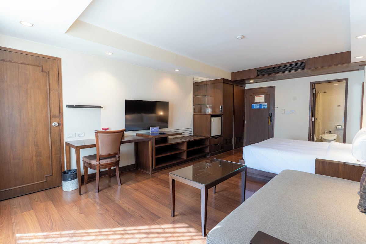 Habitación de hotel con cama, escritorio con silla, televisor, minibar y baño.
