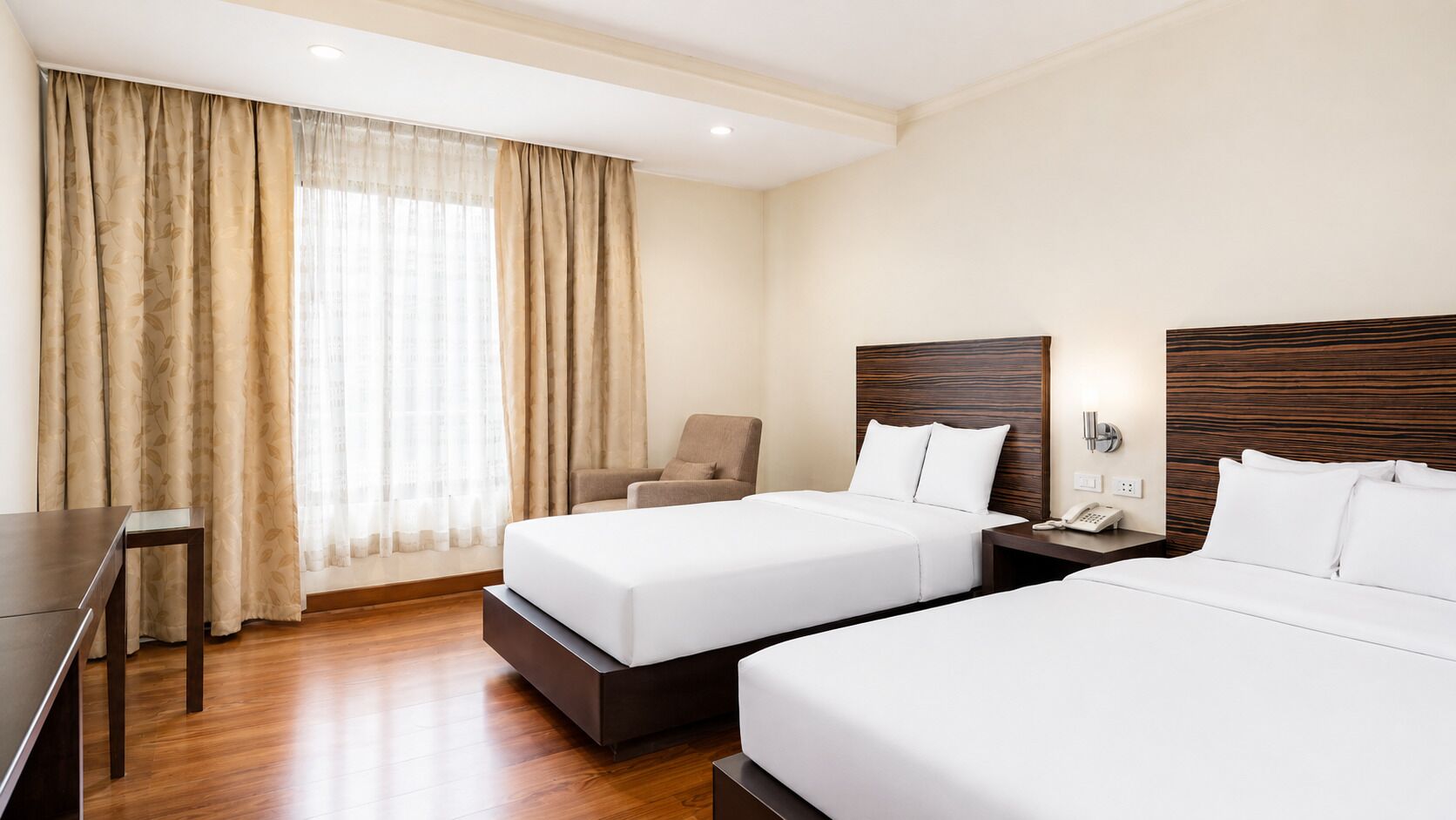A hotel room with two beds, a desk, and a chair.
