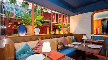 Interior de restaurante con zona de estar con bancos de madera, una mesa preparada para comer y vistas a la calle a través de amplios ventanales.