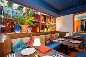 Interior de restaurante con zona de estar con bancos de madera, una mesa preparada para comer y vistas a la calle a través de amplios ventanales.