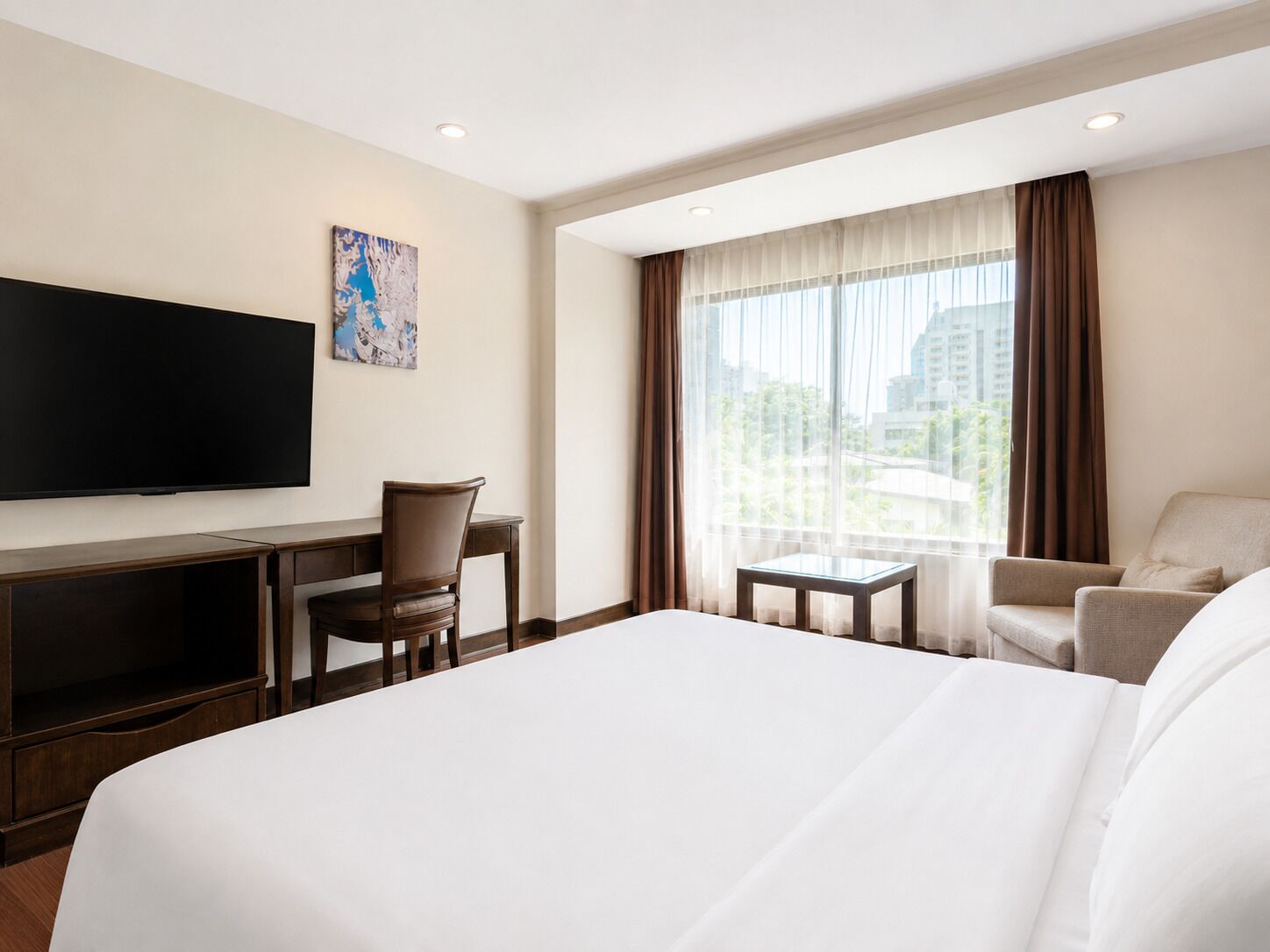 Habitación de hotel con una cama grande, un escritorio con silla, televisión y ventana con cortinas.