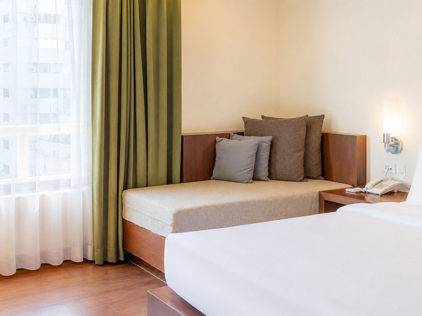 A hotel room with a bed, a bedside table with a phone, and a window with curtains.