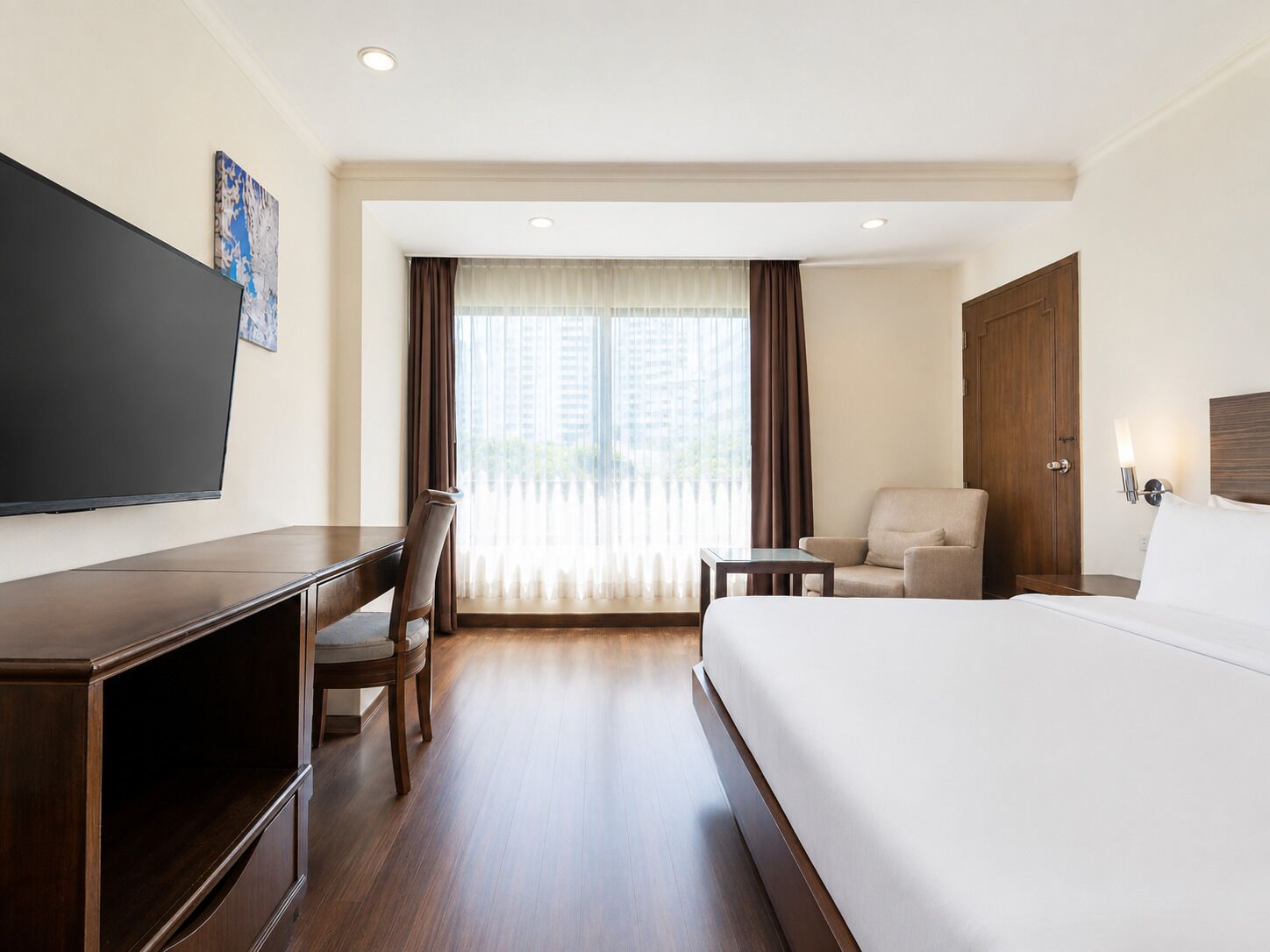 A hotel room with a bed, a desk, a chair, a television, and a window with curtains.