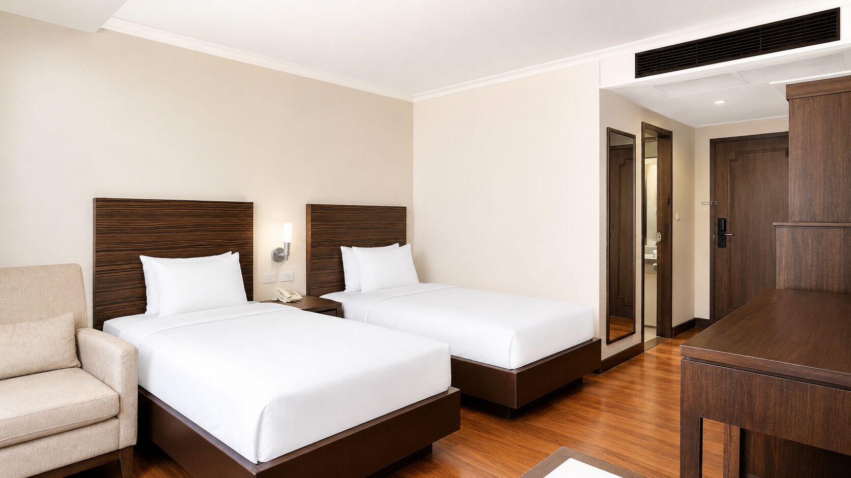 A hotel room with two beds, a desk, a chair, and a mirror.