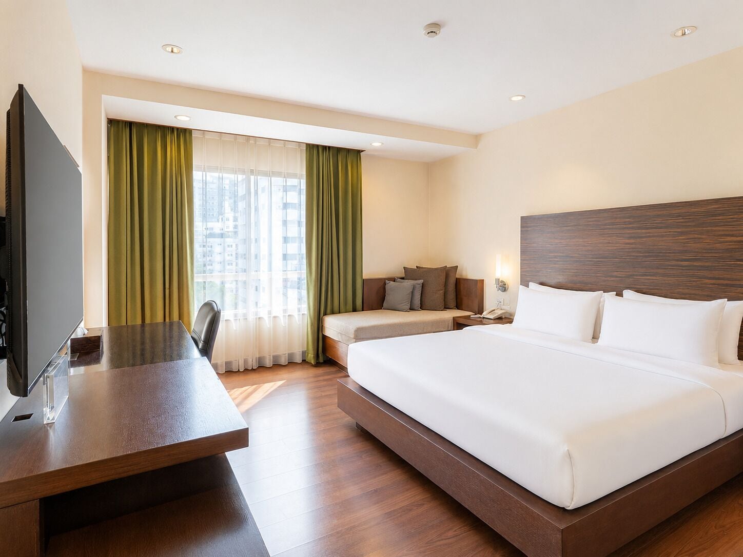 A hotel room with a large bed, a desk, a television, and a window with curtains.