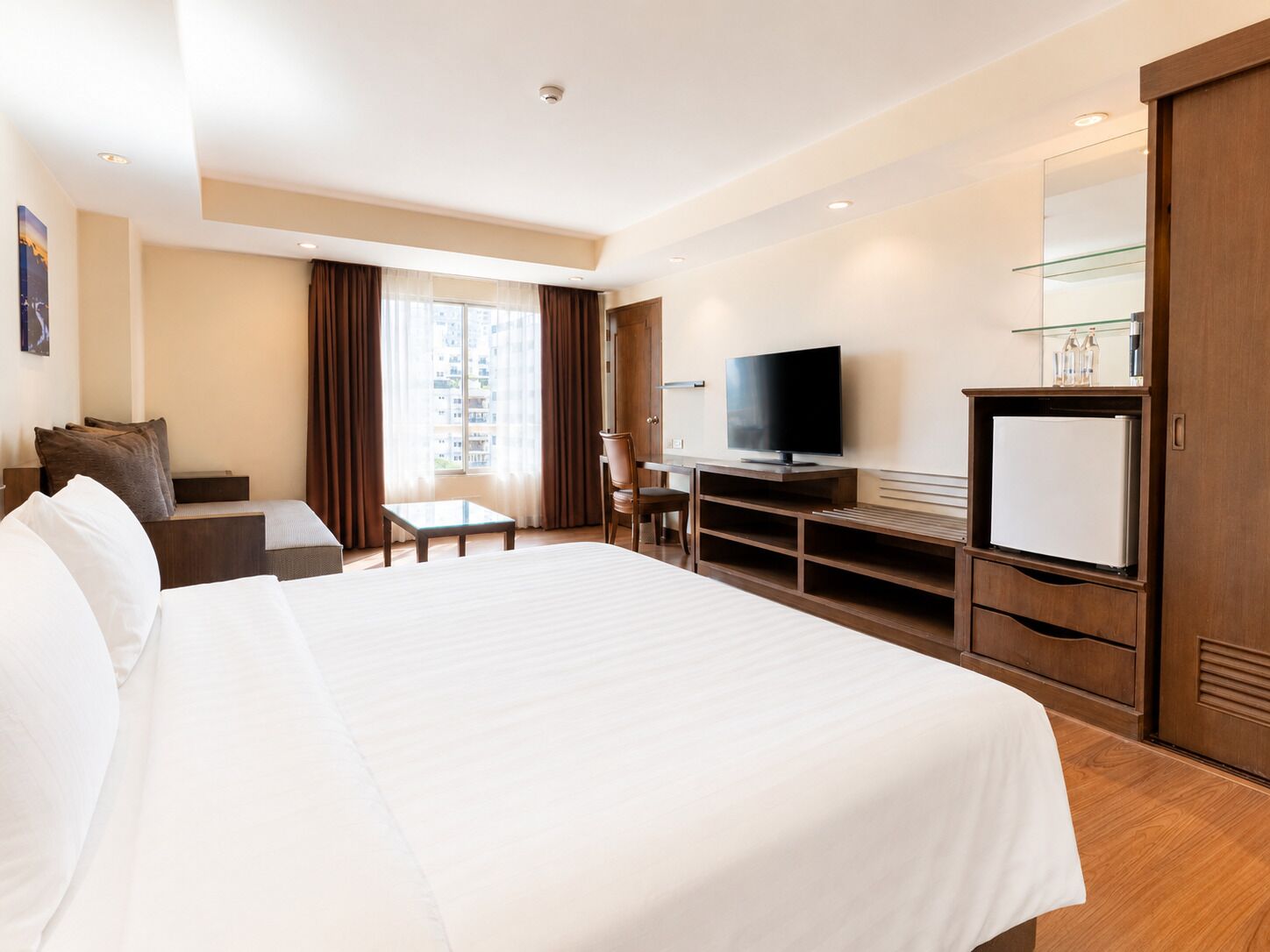 A hotel room with a large bed, a desk, a television, and a minibar.