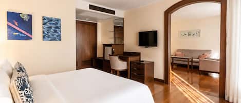 A hotel room with a bed, a desk, a television, and a seating area with a sofa and armchairs.