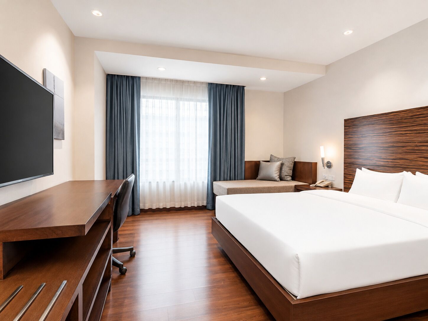 Habitación de hotel con una cama grande, un escritorio con silla, televisión y ventana con cortinas.