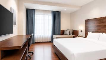 Habitación de hotel con una cama grande, un escritorio con silla, televisión y ventana con cortinas.