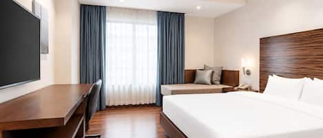 A hotel room with a large bed, a desk with a chair, a television, and a window with curtains.
