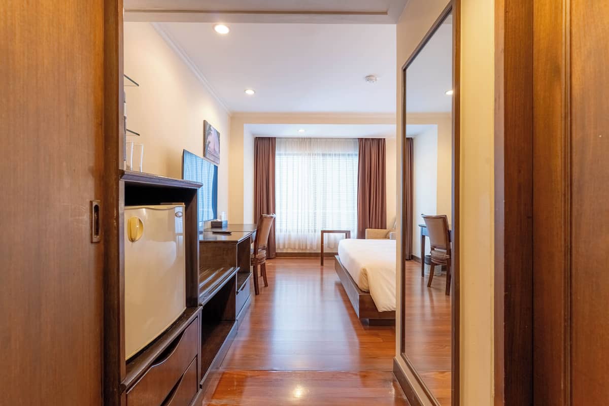 Habitación de hotel con piso de madera, una cama, un escritorio con silla, televisor y espejo.