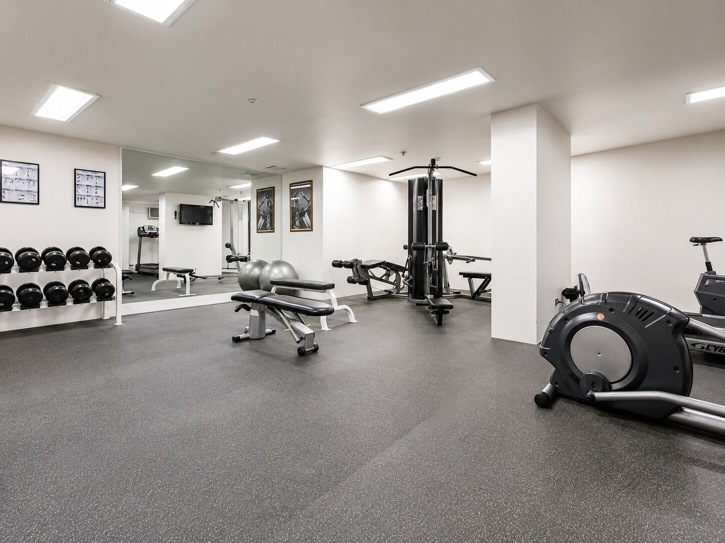 A gym with exercise equipment, a bench, and a wall-mounted dumbbell rack.
