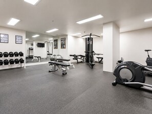 Un gimnasio con equipo de ejercicio, una banca y un soporte para pesas en la pared.