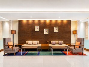 Un hall d’entrée moderne avec deux canapés, une table basse et deux fauteuils. Des tableaux encadrés ornent le mur, et une lampe sur pied est placée de chaque côté.