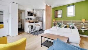 Ett modernt hotellrum med en säng, ett litet skrivbord, en stol, ett bord och ett litet pentry.