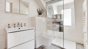 A modern bathroom with a white vanity, a toilet, a glass shower enclosure, and a large mirror. - Quiet studio - 2P - Sentier (Paris)