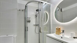 Ein modernes Badezimmer mit einer gläsernen Duschkabine, einem weißen Waschbecken und einem großen Spiegel.