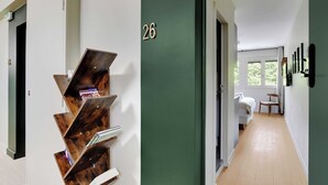 Ein Flur mit einer grünen Tür, die mit der Nummer 26 gekennzeichnet ist, der zu einem Zimmer mit Bett, Stuhl und Fenster führt.