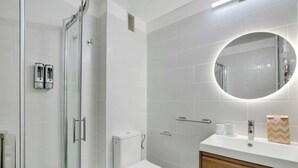 Une salle de bain moderne avec une douche à parois de verre, des toilettes blanches, un meuble-lavabo avec un miroir et un porte-serviettes.