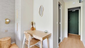 Une chambre moderne avec un bureau en bois, une chaise, une petite table ronde et un vase contenant des fleurs séchées.