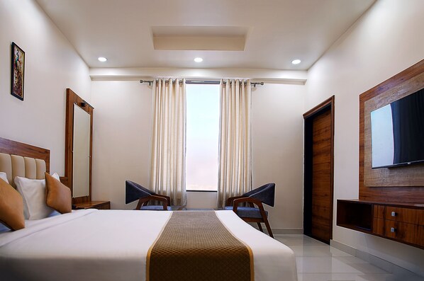 Habitación de hotel con una cama grande, dos sillas, un televisor y una ventana con cortinas.