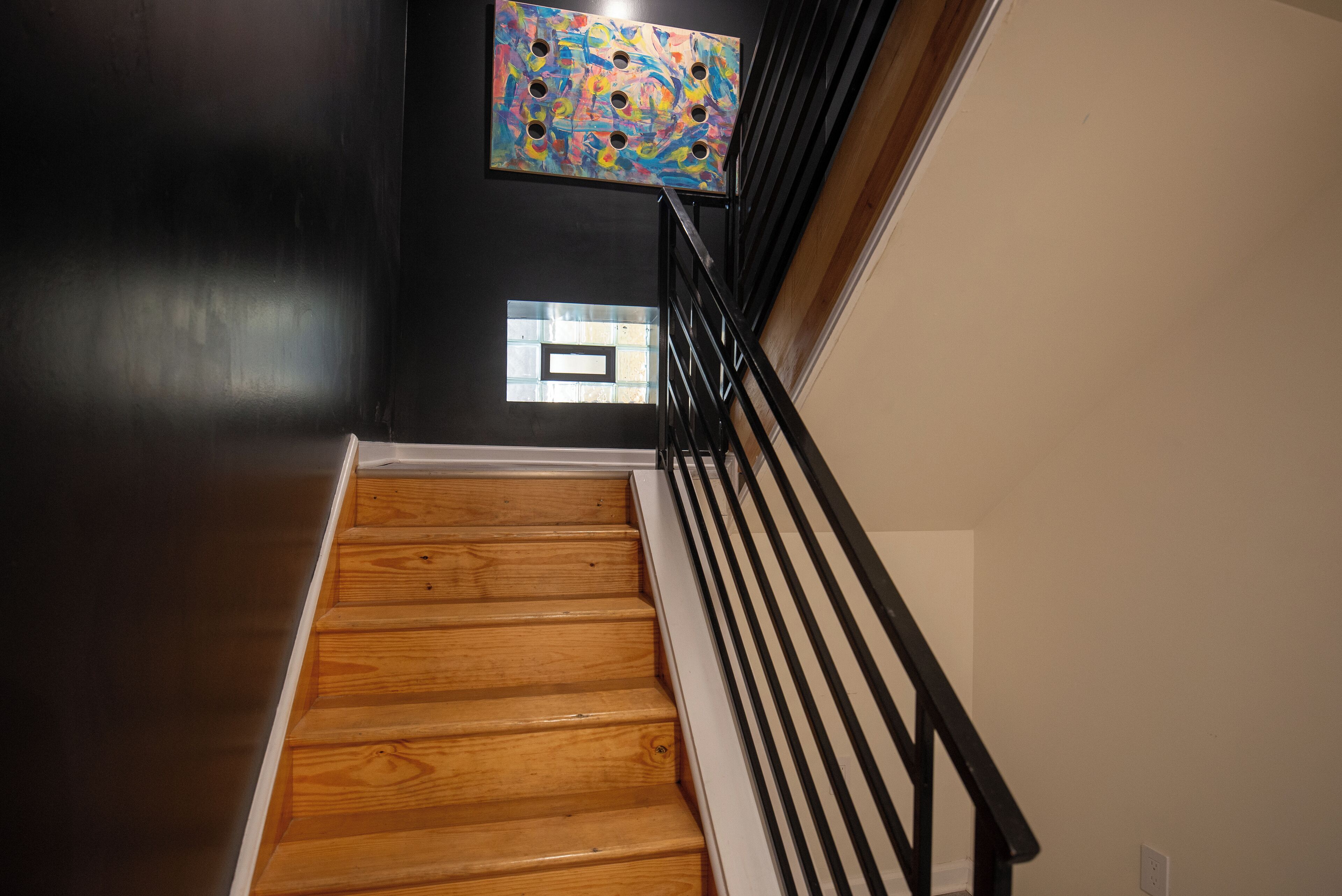 Una escala de fusta amb baranes negres, un mur negre i un quadre abstracte i colorit a la paret.