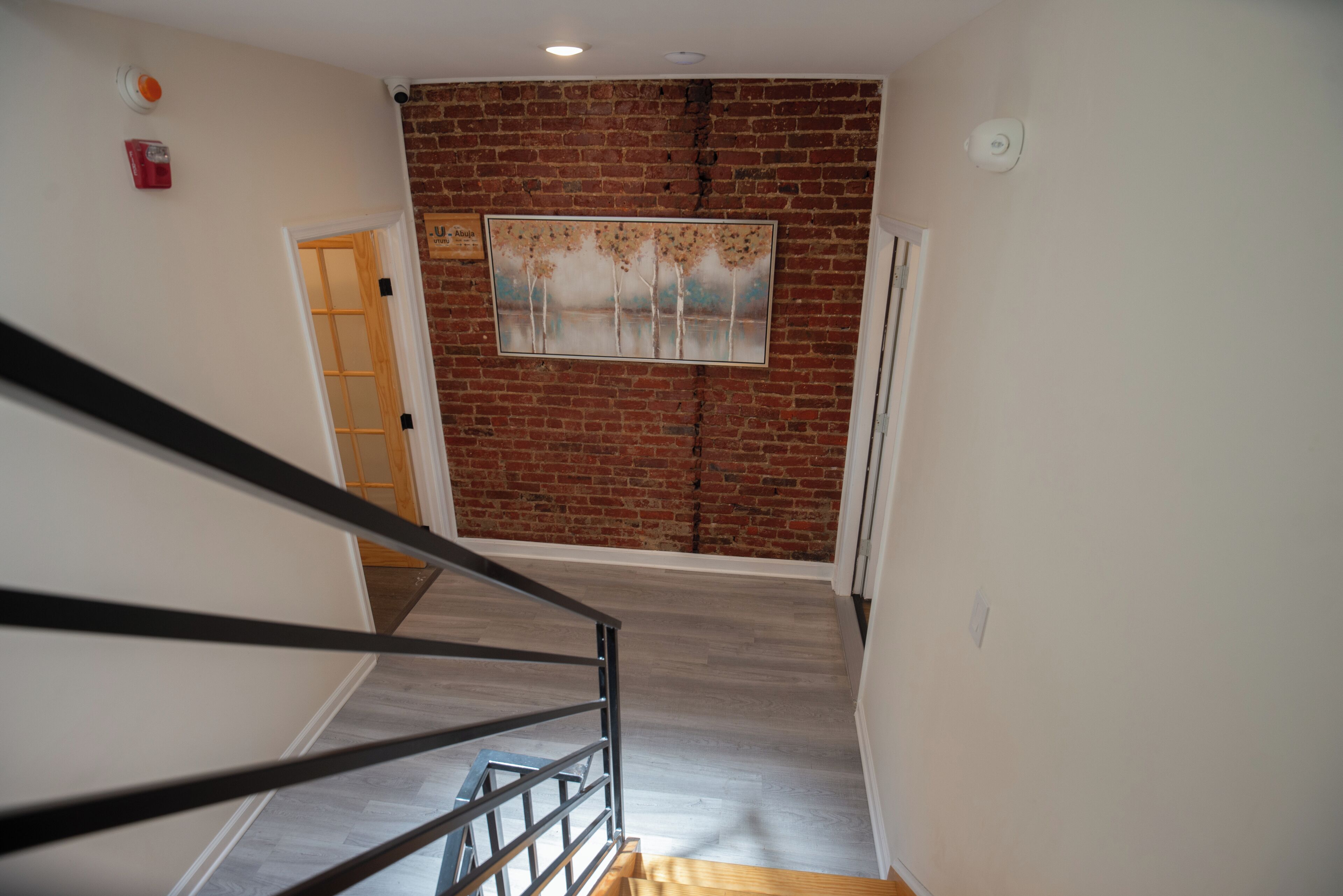 Un escalier avec une rampe en bois menant à une pièce dont un mur est en briques et qui contient un tableau encadré.