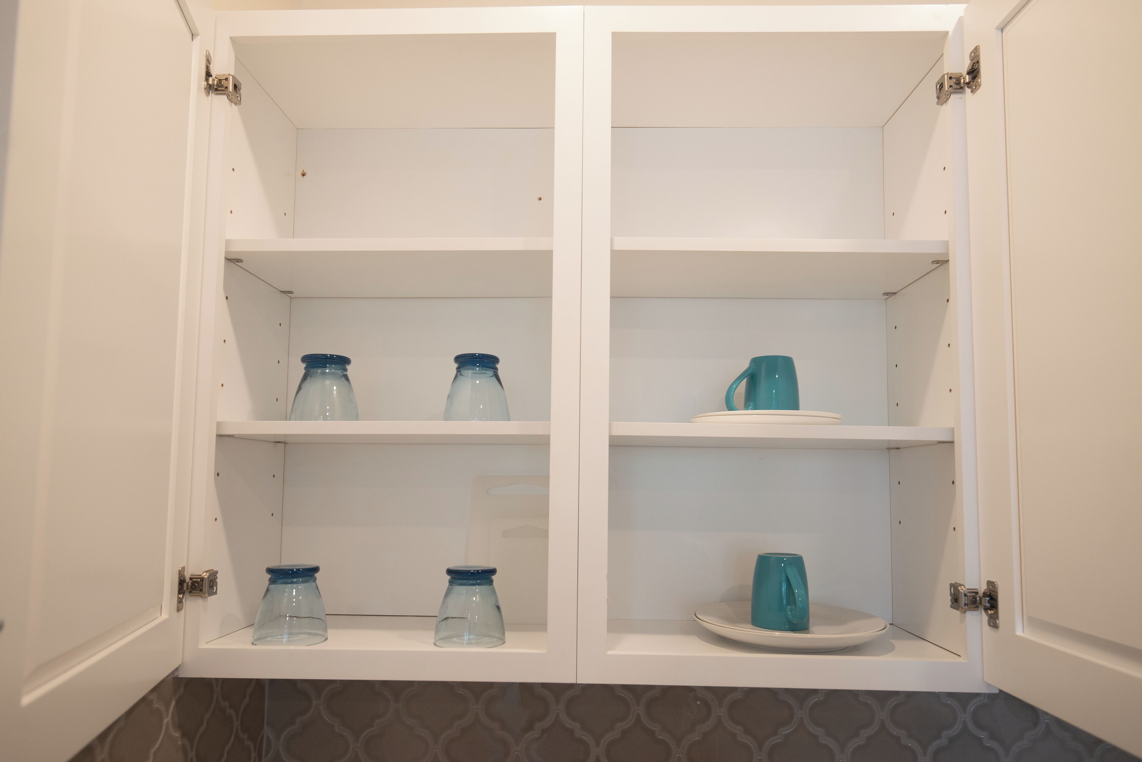 A white cabinet with two shelves, each containing a blue glass jar and a white plate.