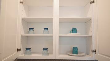 A white cabinet with two shelves, each containing a blue glass jar and a white plate.