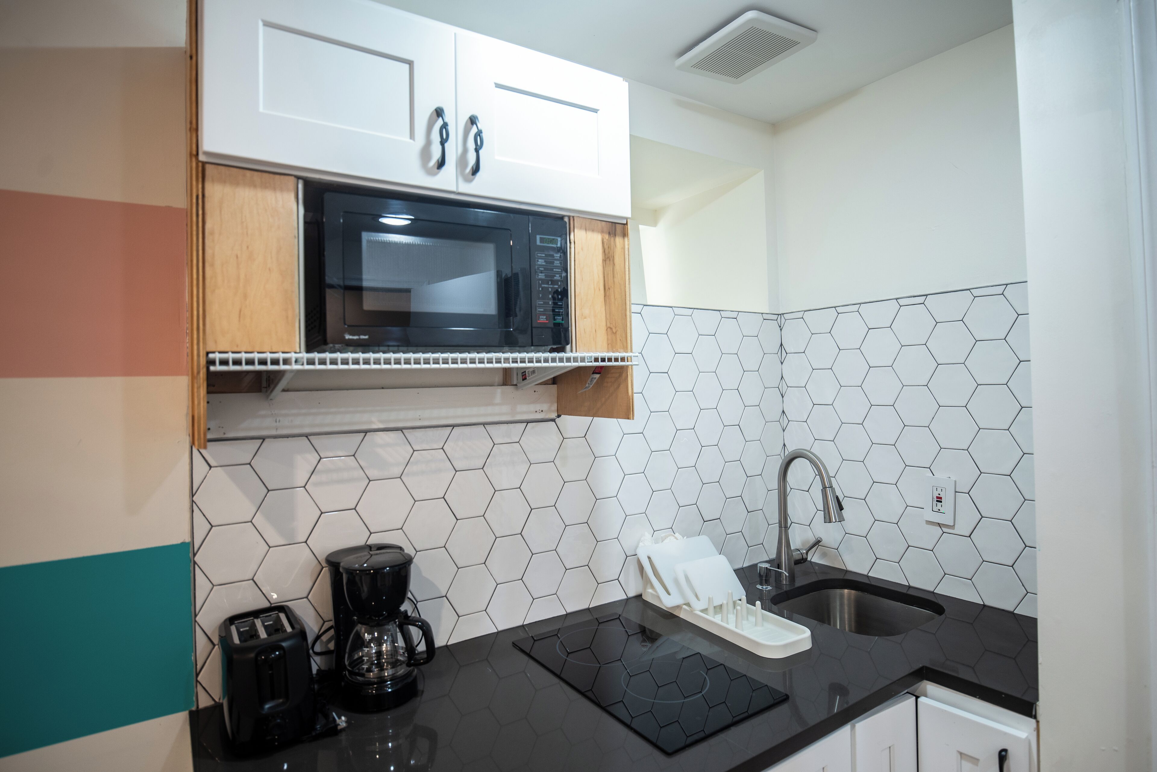 Una cocina moderna con microondas, tostadora y cafetera sobre la encimera, un fregadero y alacenas arriba.