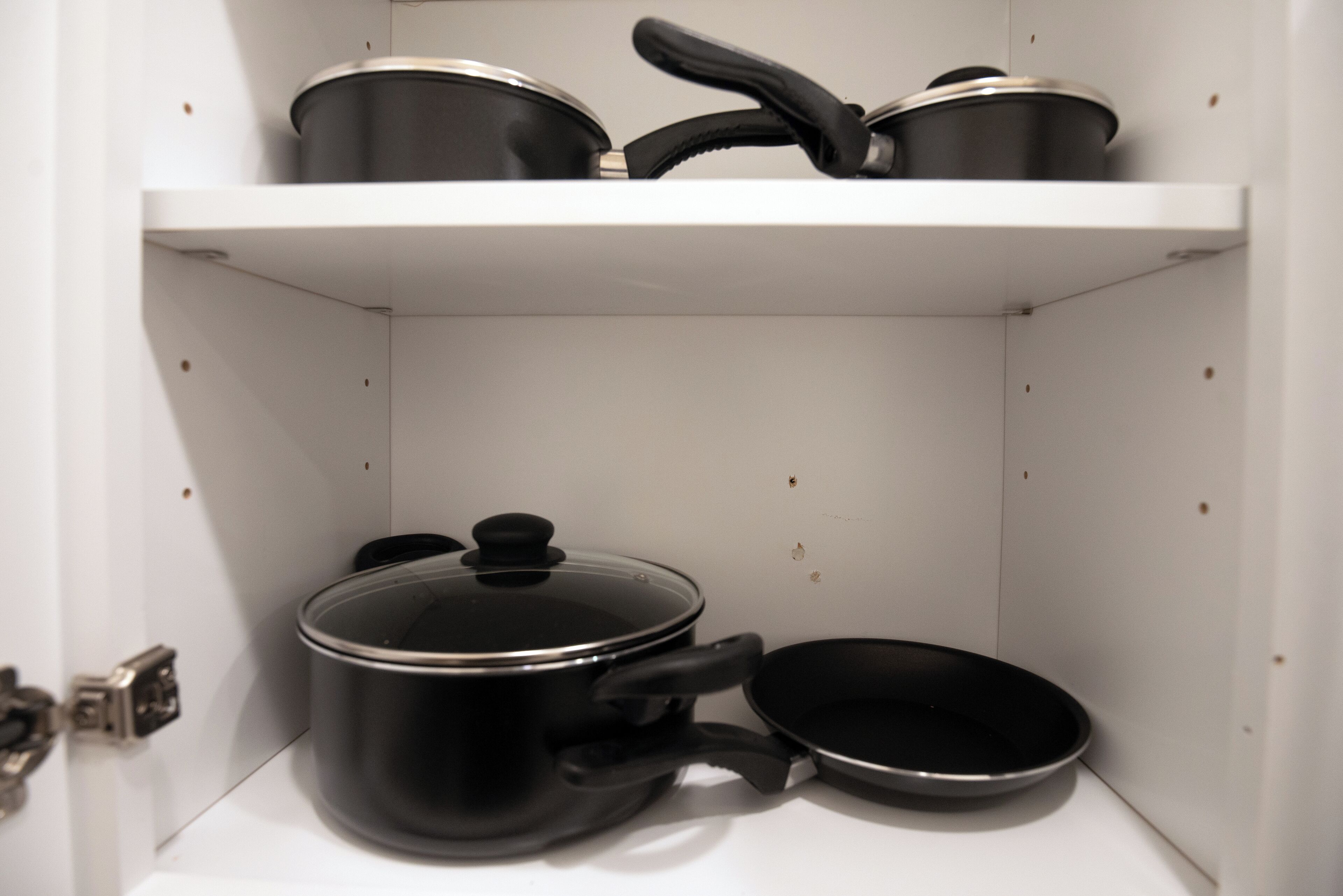 Une cuisine avec un meuble blanc contenant des ustensiles de cuisine noirs, notamment une casserole et une poêle.