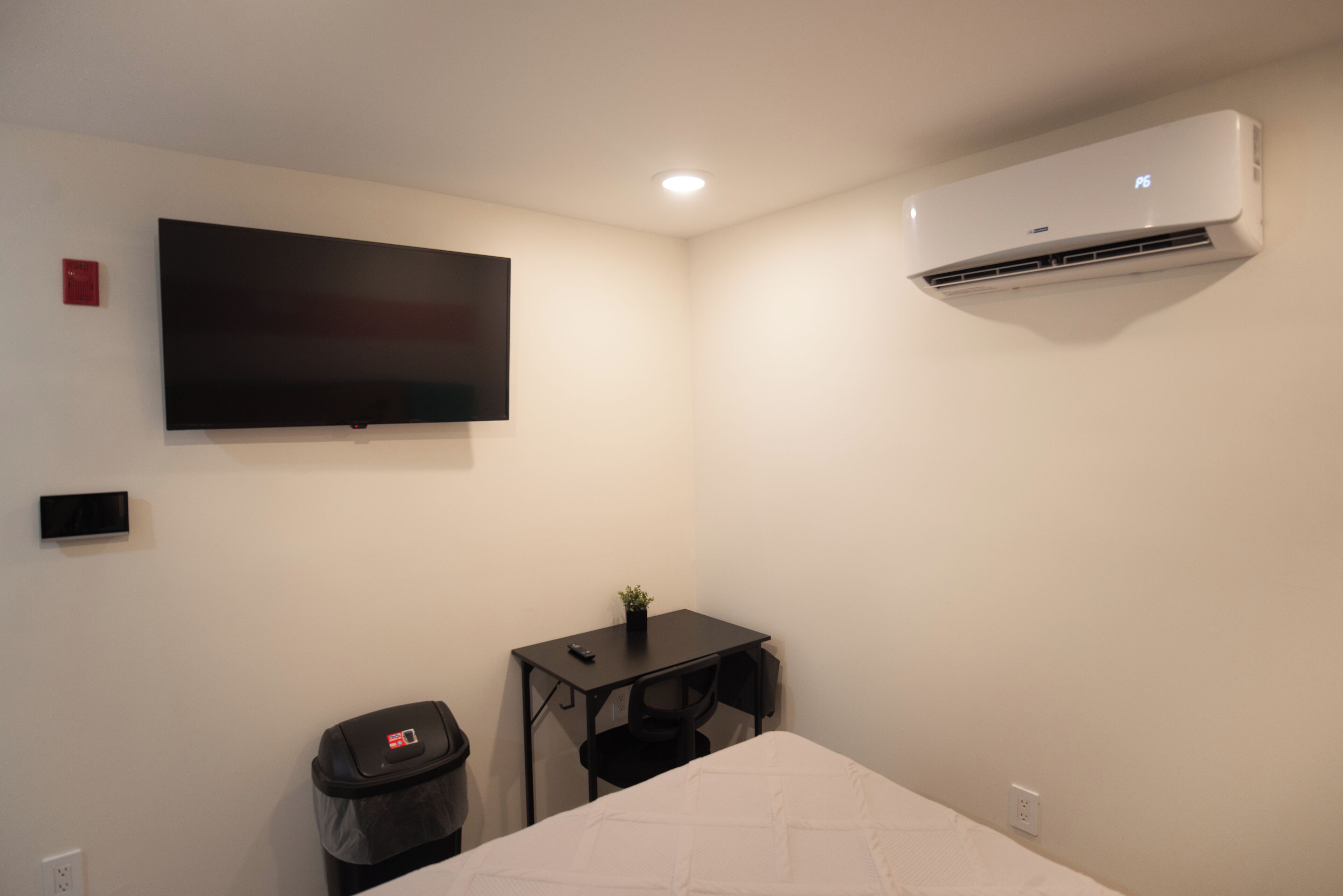 A small, clean room with a bed, a desk, a TV, and an air conditioner.