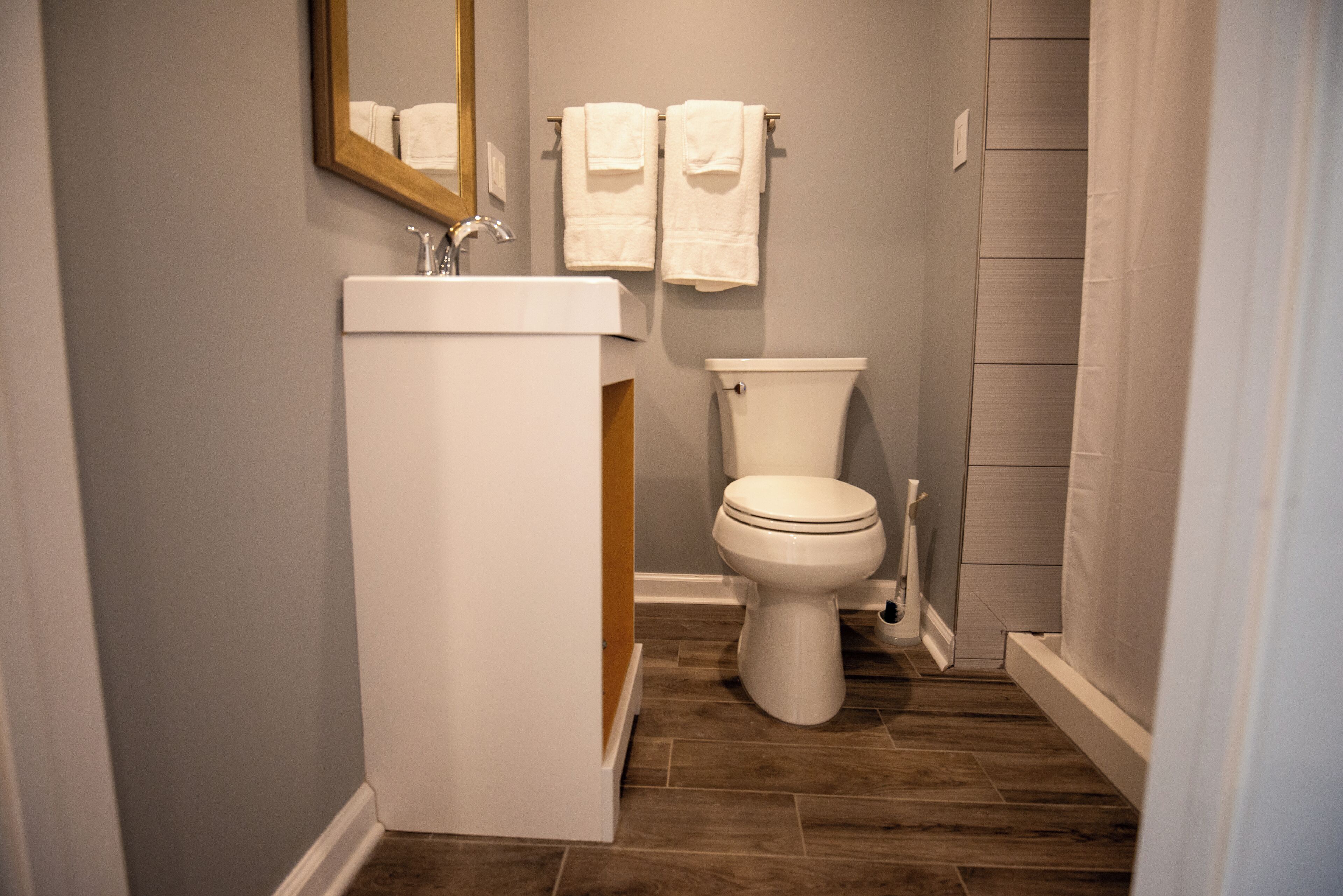 Un baño con lavamanos blanco, inodoro y suelo de madera.