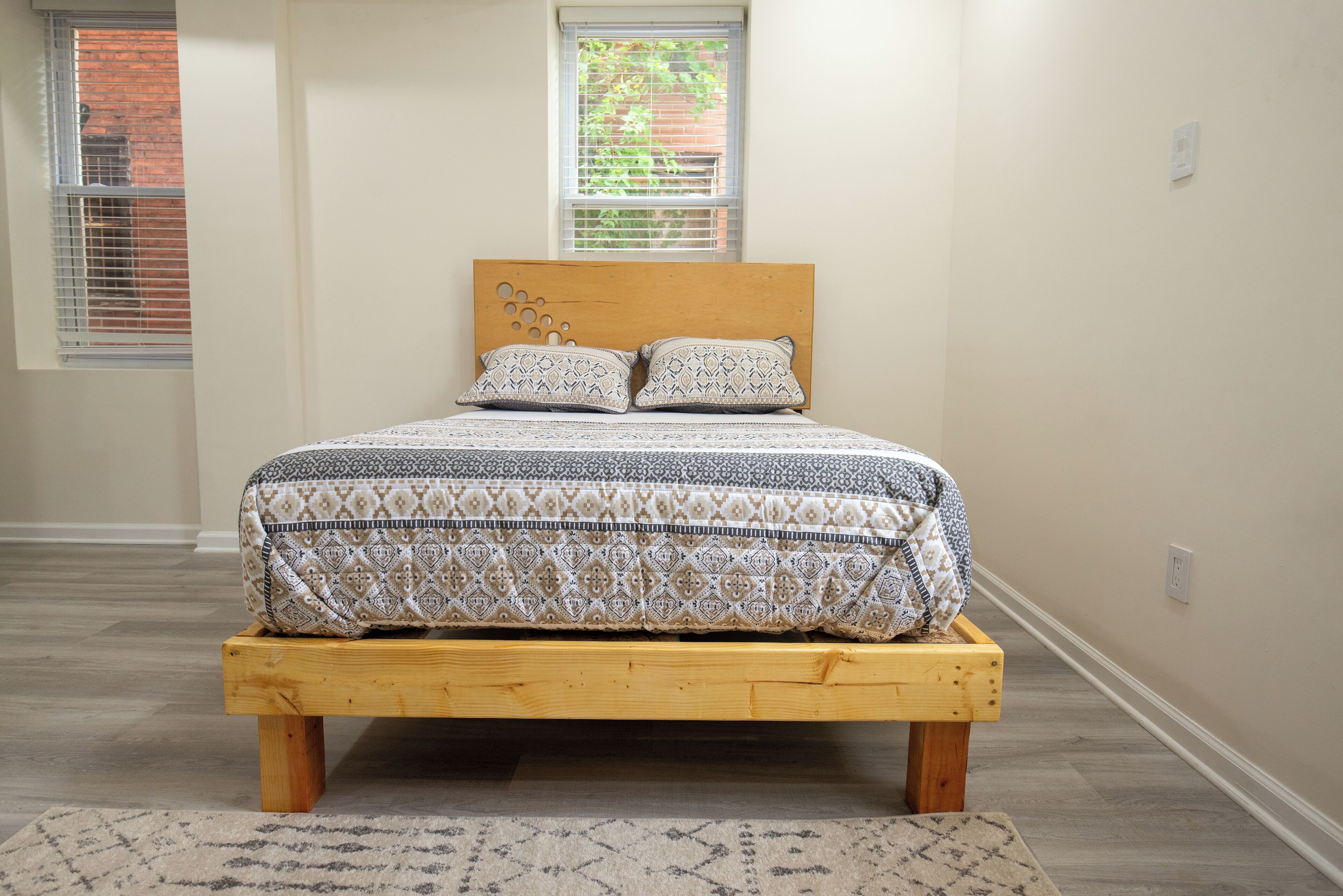 Un lit avec une couvre-lit à motifs et deux oreillers, une tête de lit en bois et un petit banc en bois placé devant le lit.