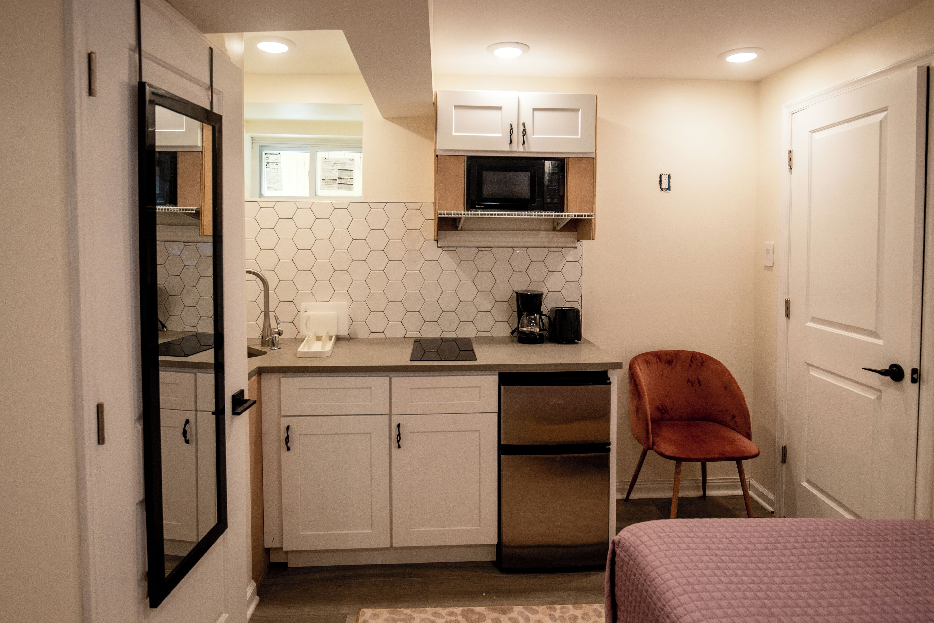 A compact kitchen with white cabinets, a microwave, a coffee maker, and a dishwasher.