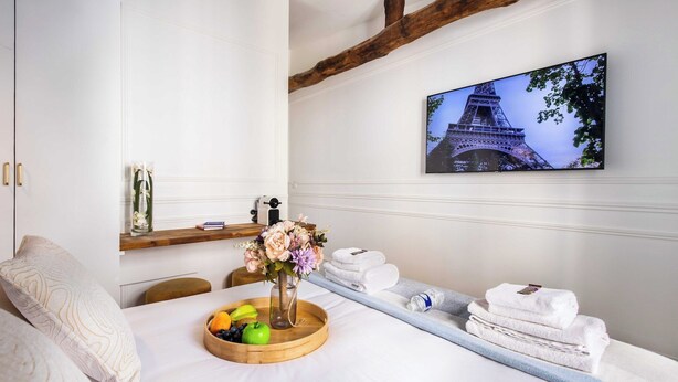 A hotel room with a bed, a wooden tray with fruits, a vase with flowers, towels, and a painting of the Eiffel Tower. - Charming private room in Pigalle (Paris)