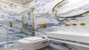 A bathroom with a marble floor, a white toilet, a glass-enclosed shower, and a gold-framed mirror. - Charming private room in Pigalle (Paris)