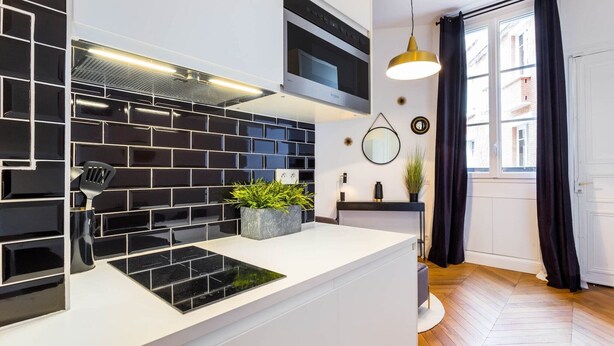 A modern kitchen with black and white tiles, a built-in stove, and a potted plant on the counter. - Elegant studio - 2P - TrocadÃ©ro / Eiffel Tower (Paris)