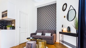 A modern living room with a grey sofa, two round coffee tables, a small ottoman, a black console table with a mirror, and a patterned wall. - Elegant studio - 2P - TrocadÃ©ro / Eiffel Tower (Paris)