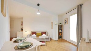 Uma sala de estar moderna com área de jantar, sofá, estante e uma janela grande com cortinas.