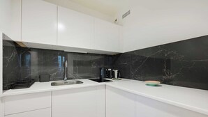 Uma cozinha moderna com armários brancos, painel de parede de mármore preto e eletrodomésticos de aço inoxidável.